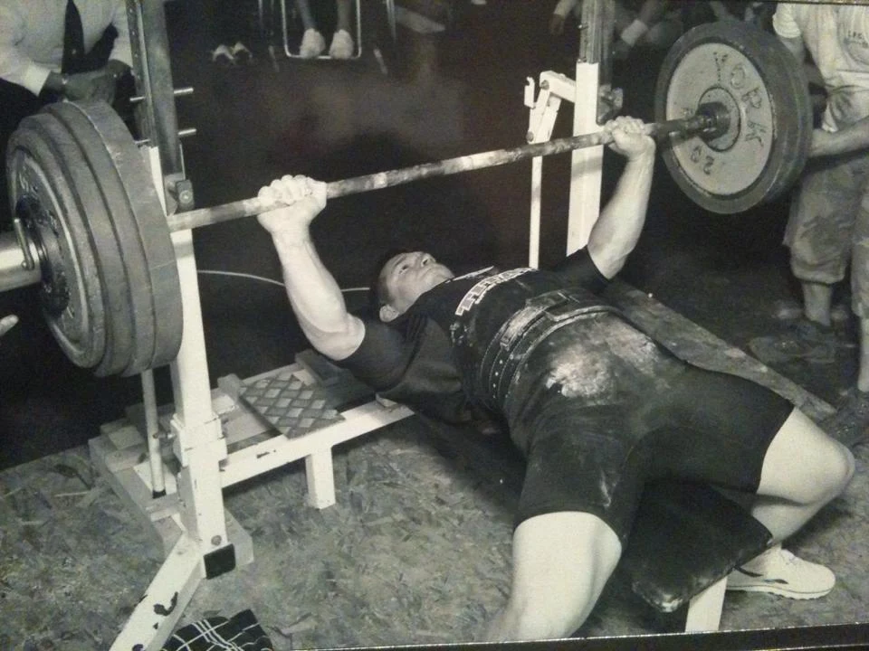 A powerlifter pressing a heavily loaded barbell in an old gritty gym